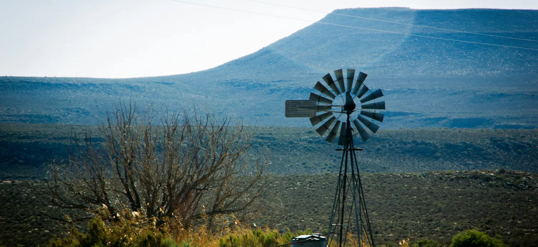 A windpump standing in dry veld beneath a flat-topped blue hill