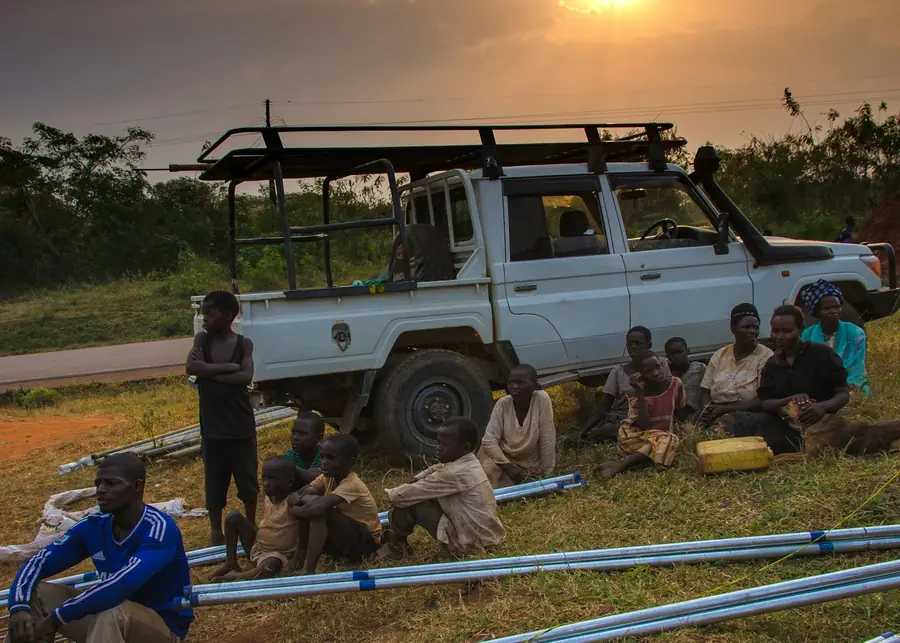 A crew resting beside lengths of blue pipe laid out on the grass at sunset